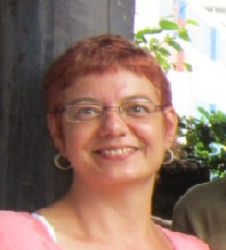 Professora Marisa da Silva Lopes. Mulher com cabelos avermelhados, lisos e curtos. Tem olhos castanhos, utiliza óculos retangulares na cor dourada. Está com blusa rosa e sorriso alegre. 