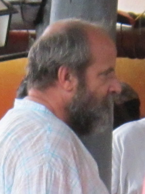 Professor Mark Julian Richter Cass. Foto de perfil, homem com cabelos grisalhos, lisos e curtos. Tem olhos castanhos, bigode grisalho, barba grisalha, cerrada e com comprimento médio. Está com camisa xadrez nas cores branca e azul-claro.  